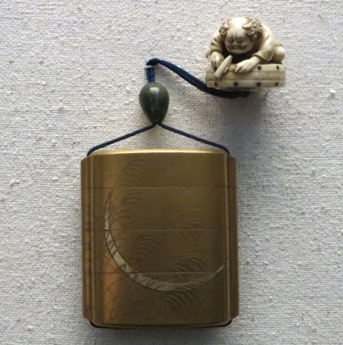 Caja o frasco metálico con un netsuke de marfil cerrando el cordón.